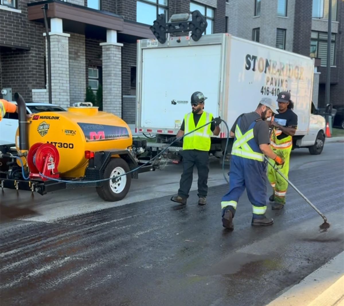 Stone-Ridge crew in safety vests finishing a freshly paved road beside new townhomes