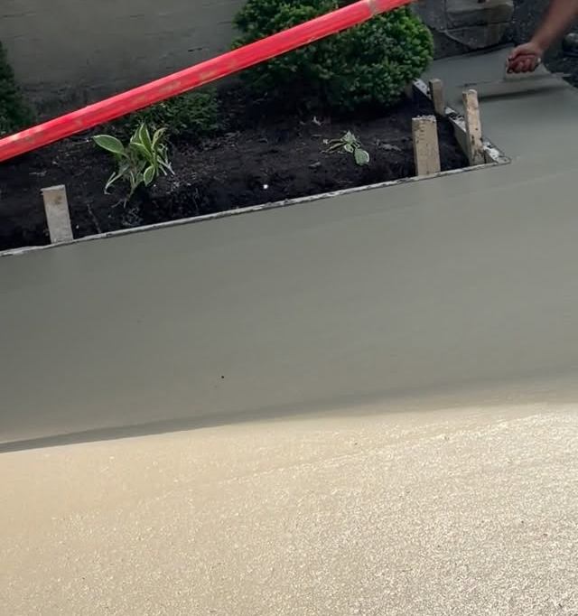 Smooth wet concrete walkway being finished beside a garden